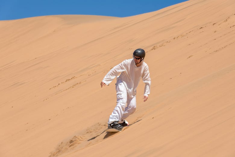 Homem praticando sandboard no deserto do Namibe